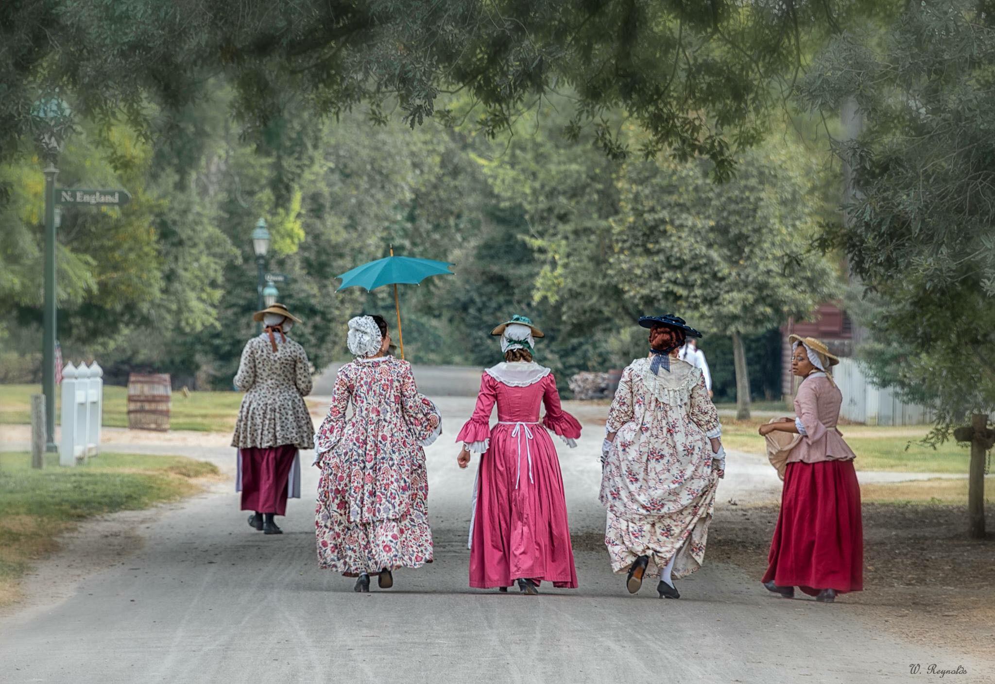 Women walk down a road in historical period dress in Colonial Williamsburg